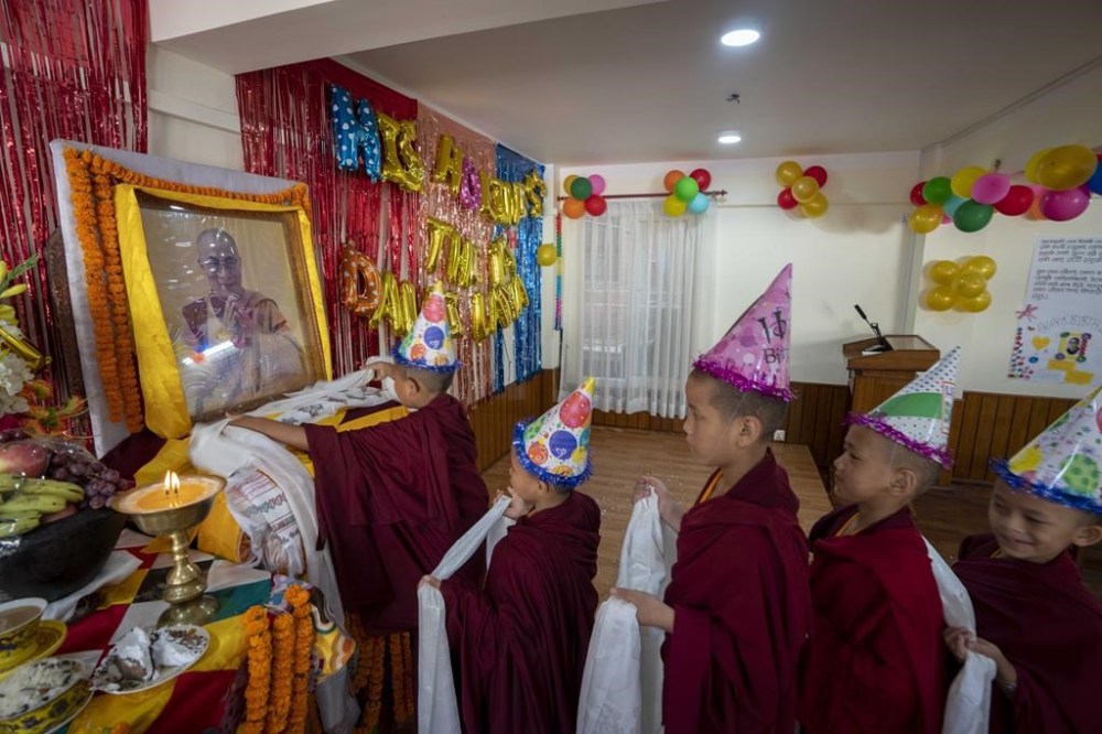 Young Buddhist monks hold ceremonial scarves and stand in queue to offer prayers in front of a portrait of their spiritual leader the Dalai Lama during his 88th birthday celebration in Kathmandu, Nepal, Thursday, July 6, 2023. (AP Photo/Niranjan Shrestha)