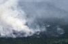 A helicopter carrying a water basket flies past a smoke plume near Lebel-sur-Quevillon, Que., Wednesday, July 5, 2023. Natural Resources Canada says the country's record-breaking wildfire season will continue to be greater than normal throughout July and into August. THE CANADIAN PRESS/Adrian Wyld