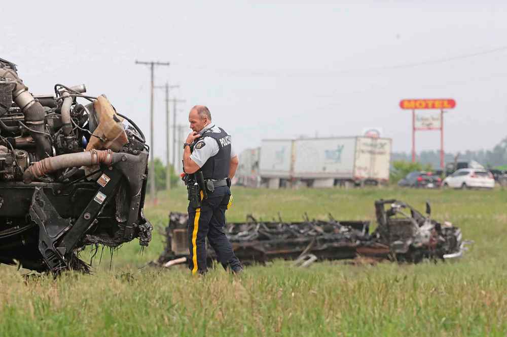 An RCMP officer walks around the semi truck while the transport bus appears in the background. (Matt Georzen / The Brandon Sun)