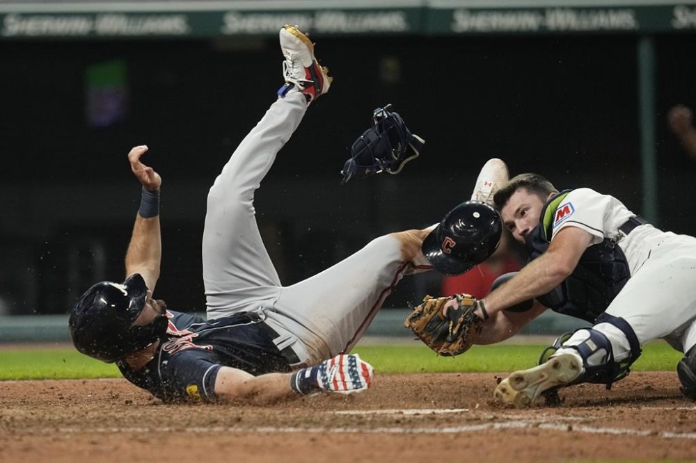 Atlanta Braves' Sam Hilliard, left, tumbles after being tagged out at home plate by Cleveland Guardians catcher David Fry, right, in the tenth inning of a baseball game Tuesday, July 4, 2023, in Cleveland. (AP Photo/Sue Ogrocki)