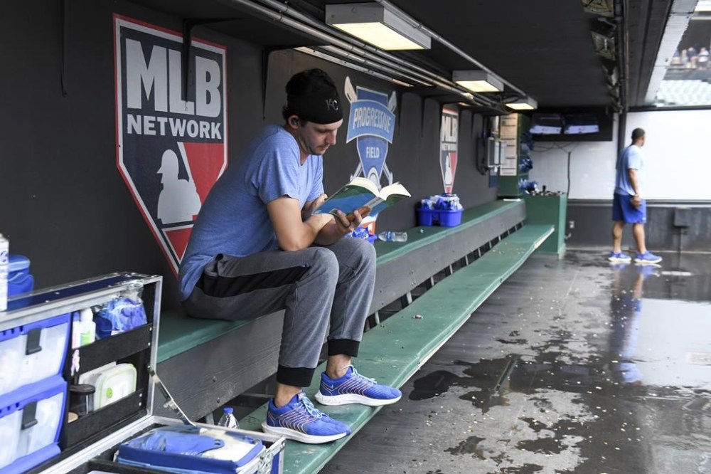 Kansas City Royals starting pitcher Daniel Lynch reads a book as a baseball game against the Cleveland Guardians is delayed due to inclement weather Saturday, July 8, 2023, in Cleveland. (AP Photo/Nick Cammett)