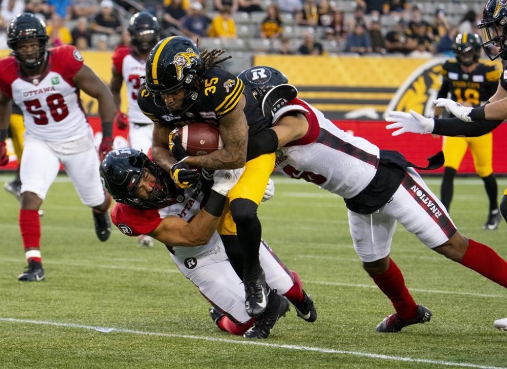 Hamilton Tiger-Cats running back Tyreik McAllister (35) is tackled by Ottawa Redblacks linebacker Adam Auclair (32) and Ottawa Redblacks defensive back Hakeem Bailey (24) during first half CFL football game action in Hamilton, Ont. on Saturday, July 8, 2023. THE CANADIAN PRESS/Peter Power