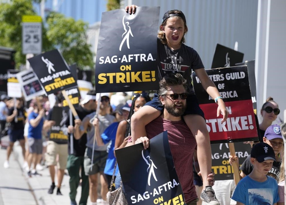 Actor Jac Cheairs and his son Wyatt, 11, take part in a rally by striking writers and actors outside Netflix studio in Los Angeles on Friday, July 14, 2023. This marks the first day actors formally joined the picket lines, more than two months after screenwriters began striking in their bid to get better pay and working conditions. (AP Photo/Chris Pizzello)