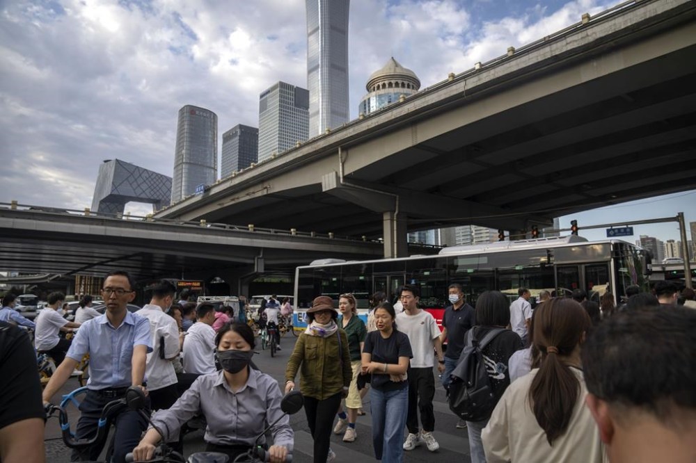 FILE - Commuters walk across an intersection during the evening rush hour in the central business district in Beijing, on June 13, 2023. China