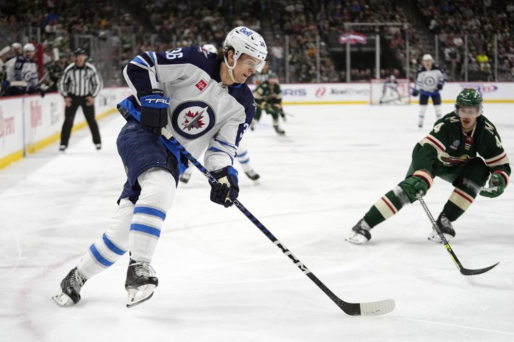 Winnipeg Jets center Morgan Barron, left, skates with the puck alongside Minnesota Wild defenseman Jon Merrill during the second period of an NHL hockey game in St. Paul, Minn., on April 11, 2023. THE CANADIAN PRESS/AP, Abbie Parr