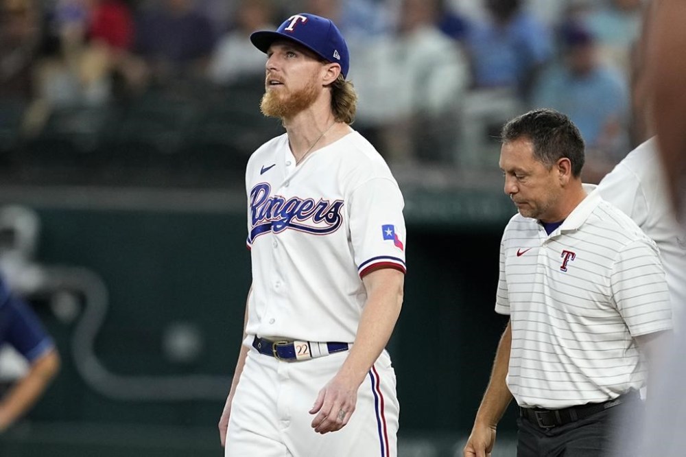 Texas Rangers starting pitcher Jon Gray looks up as head athletic trainer Matt Lucero, right, checks on him after Gray was hit by a single off the bat of Tampa Bay Rays' Yandy Diaz in the fifth inning of a baseball game, Wednesday, July 19, 2023, in Arlington, Texas. Gray left the game with an unknown leg injury. (AP Photo/Tony Gutierrez)