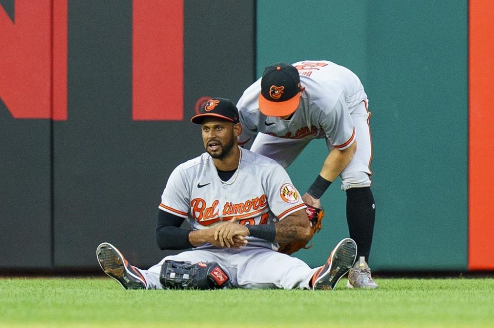 Baltimore Orioles center fielder Aaron Hicks, left, grabs his hand after catching the line-out by Philadelphia Phillies' Johan Rojas as Austin Hays, right, tries to help him up during the third inning of a baseball game, Monday, July 24, 2023, in Philadelphia. (AP Photo/Chris Szagola)