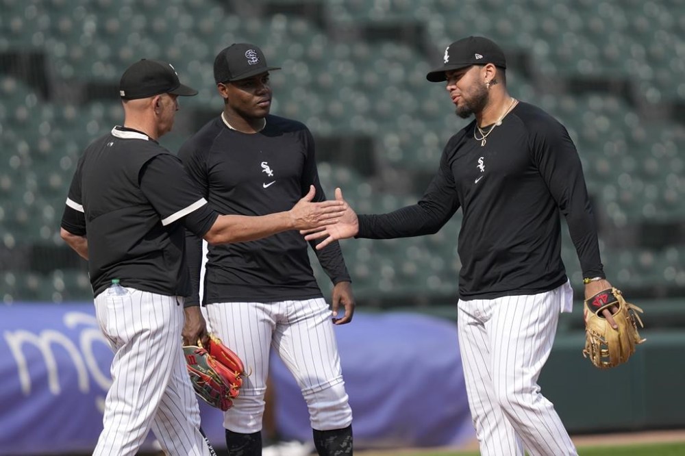 Chicago White Sox manager Pedro Grifol, left, shakes hands with Yoán Moncada as Oscar Colas watches, during infield practice before the team's baseball game against the Chicago Cubs, Tuesday, July 25, 2023, in Chicago. Moncada returned to the team after an injury rehabilitation assignment, reinstating him from the 10-day injured list. (AP Photo/Charles Rex Arbogast)