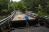 A warming climate is causing seas to rise and storms to become more severe with waters encroaching on roads and bridges, leading to flooding. Ron Crawford climbs up a ladder onto a washed-out bridge after checking on stranded neighbours near McKay Section, N.S. on Sunday, July 23, 2023. THE CANADIAN PRESS/Darren Calabrese