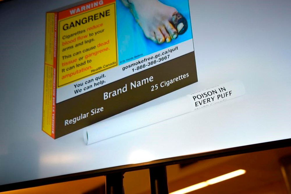 New Health Canada regulations that require warning labels to be printed on individual cigarettes are coming into effect tomorrow. An example of cigarette packaging with expanded warnings, including a warning printed on the cigarettes themselves, is shown on a screen after a news conference, in Ottawa, Friday, June 10, 2022. THE CANADIAN PRESS/Justin Tang