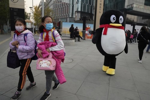 Children pass by a mascot for Tencent during a promotion event in Beijing, on Nov. 11, 2020. On Wednesday, Aug. 2, 2023, China's internet watchdog has laid out regulations to curb the amount of time minors spend on their smartphones, in the latest blow to firms such as Tencent and ByteDance which run social media platforms and online games. (AP Photo/Ng Han Guan)
