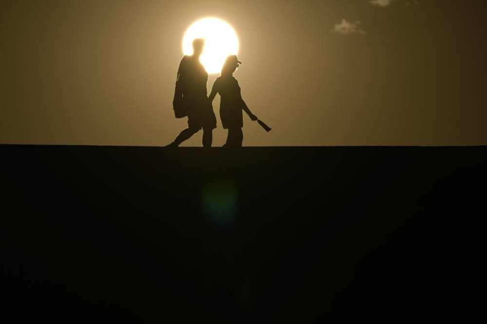 FILE - People walk along a trail as the sun sets, July 16, 2023, in Death Valley National Park, Calif. Across the U.S., many people are living through one of the most brutal summers of their lives and reckoning with the idea that climate change is only going to make matters worse in the coming decades. (AP Photo/John Locher, File)