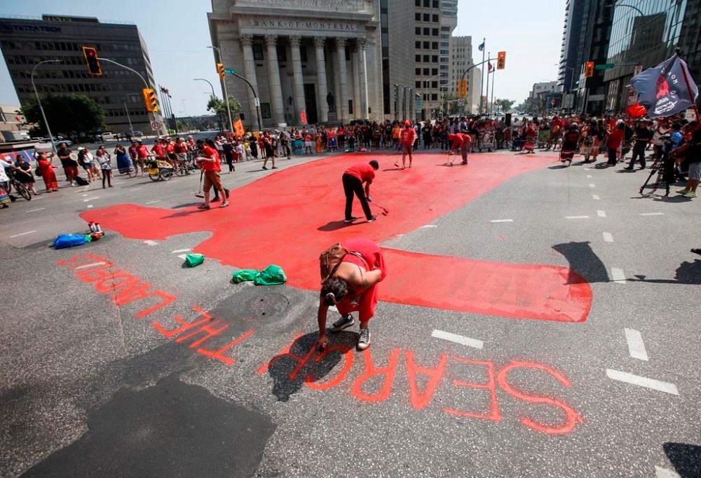 Family and supporters paint a red dress in Winnipeg on Thursday, Aug. 3, 2023, as they gathered to protest the lack of action from all levels of governments in funding a search of a landfill for missing Indigenous women. THE CANADIAN PRESS/John Woods