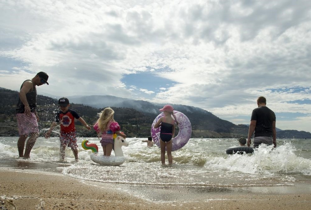 Beach goers play in the waves of Skaha Lake in Penticton, B.C. Friday, Aug. 21, 2020. Police in British Columbia say one teen is dead after a Jet Ski collision on Skaha Lake.  THE CANADIAN PRESS/Jonathan Hayward