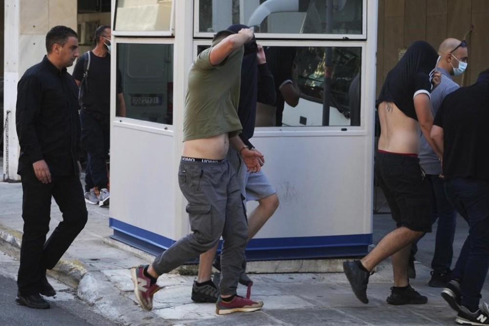 Soccer fans covering their faces, most of them from Croatia, are escorted by police as they leave the Athens Police Headquarters, Greece, Wednesday, Aug. 9, 2023. Ninety-four fans of Croatia's Dinamo Zagreb are appearing in court this morning for a preliminary hearing over Monday night's fan violence that left a fan of Greece's AEK dead and another eight people injured. (AP Photo/Petros Giannakouris)