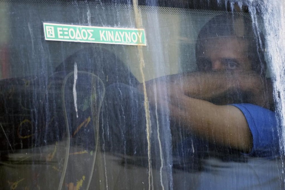 A soccer fan sits inside a police bus upon his departure from the Athens Police Headquarters, Greece, Wednesday, Aug. 9, 2023. Ninety-four fans of Croatia's Dinamo Zagreb are appearing in court this morning for a preliminary hearing over Monday night's fan violence that left a fan of Greece's AEK dead and another eight people injured. The sign on the window reads