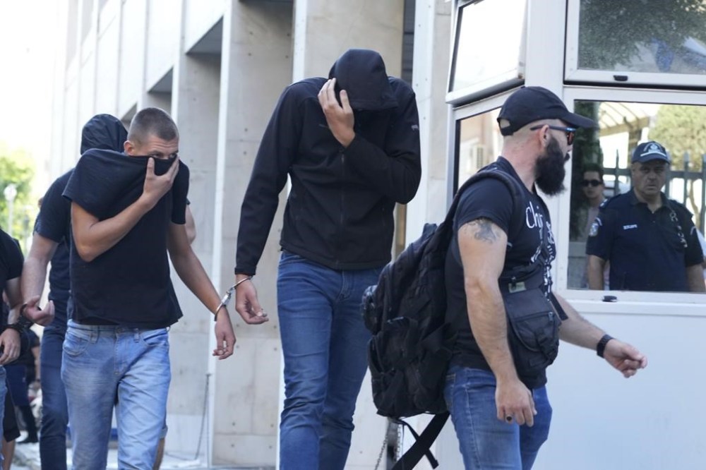 Soccer fans covering their faces, most of them from Croatia, are escorted by police as they leave the Athens Police Headquarters, Greece, Wednesday, Aug. 9, 2023. Ninety-four fans of Croatia's Dinamo Zagreb are appearing in court this morning for a preliminary hearing over Monday night's fan violence that left a fan of Greece's AEK dead and another eight people injured. (AP Photo/Petros Giannakouris)