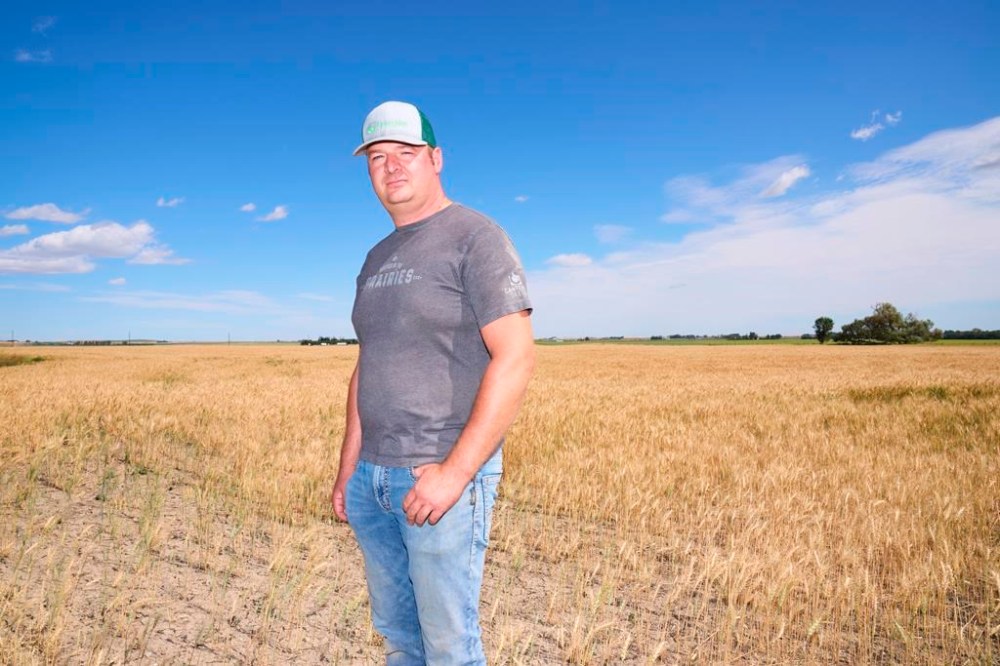 Farmer Sean Stanford poses in his wheat field near Magrath, Alta. on Tuesday, July 25, 2023. Stanford's wheat farm just south of Lethbridge, Alta. could have been struggling amid a dry spring and summer. But Stanford is growing crops, thanks to a series of small sprinklers, attached to a large pipe and powered by an electric motor that disperse water from a nearby irrigation canal over some of his fields. THE CANADIAN PRESS/Todd Korol