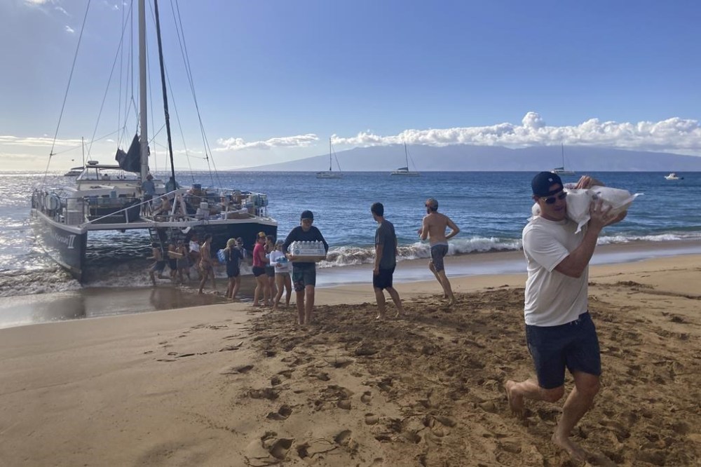 A group of volunteers who sailed from Maalaea Bay, Maui, form an assembly line on Kaanapali Beach on Saturday Aug. 12, 2023, to unload donations from a boat. Maui residents have come together to donate water, food and other essential supplies to people on the western side of the island after a deadly fire destroyed hundreds of homes and left scores of people homeless. (AP Photo/Rick Bowmer)