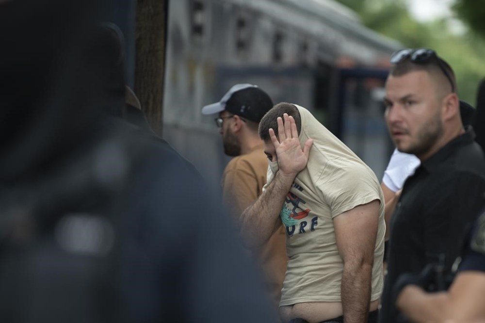 A soccer fan covers his face as the police escort him from the General Police Directorate of Attica to court, in Athens, Greece, Sunday, Aug. 13, 2023. A 29-year-old AEK Athens fan died from a stab wound, and ten others were injured when scores of Croatian supporters wielding wooden clubs and metal bats attacked bystanders outside AEK's Opap Arena on Monday. (AP Photo/Michael Varaklas)