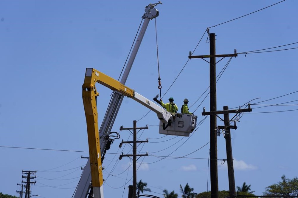 FILE - Linemen work on poles, Sunday, Aug. 13, 2023, in Lahaina, Hawaii, following a deadly wildfire that caused heavy damage days earlier. Hawaiian Electric Co. faces criticism for not shutting off the power amid high wind warnings and keeping it on even as dozens of poles began to topple. (AP Photo/Rick Bowmer, File)