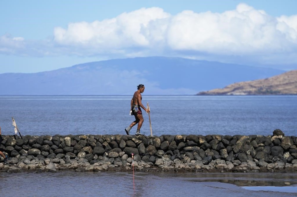 Vicente Ruboi walks along a sea wall, Tuesday, Aug. 15, 2023, in Kihei, Hawaii, following wildfires that ravaged Maui. (AP Photo/Rick Bowmer)