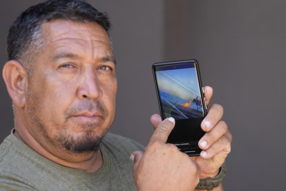 Shane Treu points to his phone while showing the video of the fire during an interview Tuesday, Aug. 15, 2023, in Wailuku, Hawaii. A video by Treu and others captured the early moments of what would become the deadliest U.S. wildfire in more than a century. (AP Photo/Rick Bowmer)