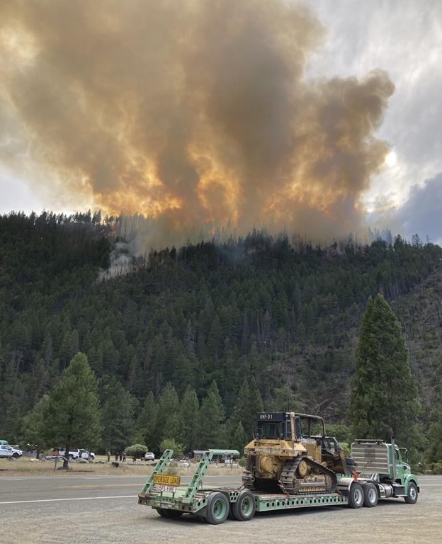 In this photo provided by Caltrans, smoke rises from the Head Fire in Klamath National Forest, Calif., on Tuesday Aug. 15, 2023. A wildfire pushed by gusty winds from a thunderstorm raced through national forest land near California's border with Oregon, prompting evacuations in the rural area. The blaze in Siskiyou County was one of at least 19 fires — most of them tiny — that erupted in the Klamath National Forest as thunderstorms rolling through the area brought lightning and downdrafts that drove the flames through timber and rural lands. (Roger Matthews/Caltrans via AP)