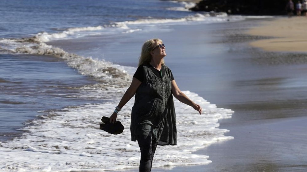 Anne Landon walks along a beach, Tuesday, Aug. 15, 2023, in Kihei, Hawaii. Landon has sought help in coping with anxiety following the devastating wildfire in Maui. Landon, 70, has twice sought help in recent days to help her cope with anxiety. One psychologist she spoke with at an evacuation shelter taught her special breathing techniques to bring her heart rate down. On another occasion, a nurse providing 24/7 crisis support at her current shelter was there to comfort her while she cried. (AP Photo/Rick Bowmer)