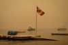 Thick smoke from the Lower East Adams Lake wildfire fills the air and a Canadian flag flies in the wind as RCMP officers on a boat patrol Shuswap Lake, in Scotch Creek, B.C., on Sunday, August 20, 2023. THE CANADIAN PRESS/Darryl Dyck