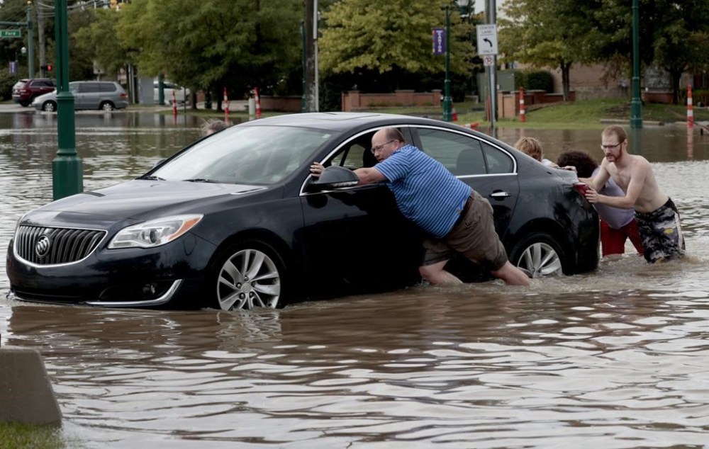 People help push a car out of floodwaters after a woman got stuck in the middle of Canton Center Road in Canton, Mich., after a thunderstorm dumped several inches of rain in the area early Thursday, Aug. 24, 2023. (Eric Seals/Detroit Free Press via AP)