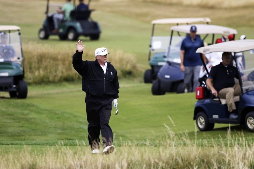 FILE — President Donald Trump waves to protesters while playing golf at Turnberry golf club in Turnberry, Scotland, Britain, July 14, 2018. (AP Photo/Peter Morrison, File)