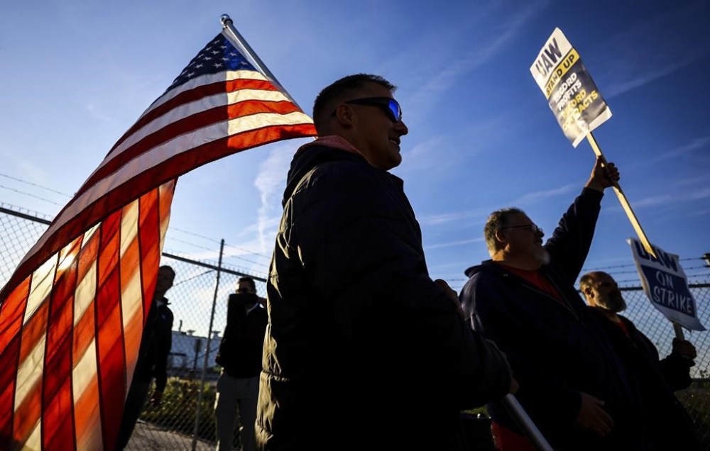 UAW members Dan Schlieman, with flag, and Brad Geer work the picket line during a strike Tuesday, Sept. 19, 2023, at the Stellantis Toledo Assembly Complex where Jeeps are made in Toledo, Ohio. (Jeremy Wadsworth/The Blade via AP)