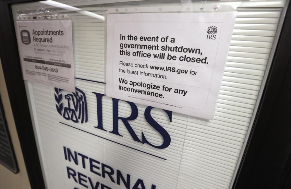 FILE - Doors at the Internal Revenue Service (IRS) in the Henry M. Jackson Federal Building are locked and covered with blinds as a sign posted advises that the office will be closed during the partial government shutdown Jan. 16, 2019, in Seattle. The federal government is heading toward a shutdown that will disrupt many services, squeeze workers and roil politics. (AP Photo/Elaine Thompson, File)