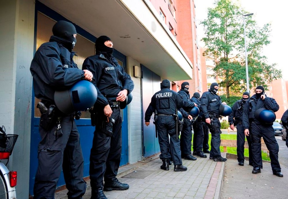 Police officers on duty during a raid stand in front of an apartment building in Stade, Germany, Tuesday Sept. 26, 2023. During a raid in five federal states, the federal police discovered several Syrians suspected of having been smuggled in early Tuesday morning. Arrest warrants had also been executed against suspected smugglers. (Daniel Bockwoldt/dpa via AP)