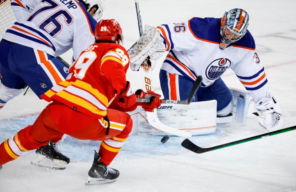 Edmonton Oilers goalie Jack Campbell, right, swats the puck away from Calgary Flames forward Dillon Dube during first period NHL pre-season hockey action in Calgary, Alta., Friday, Sept. 29, 2023. THE CANADIAN PRESS/Jeff McIntosh