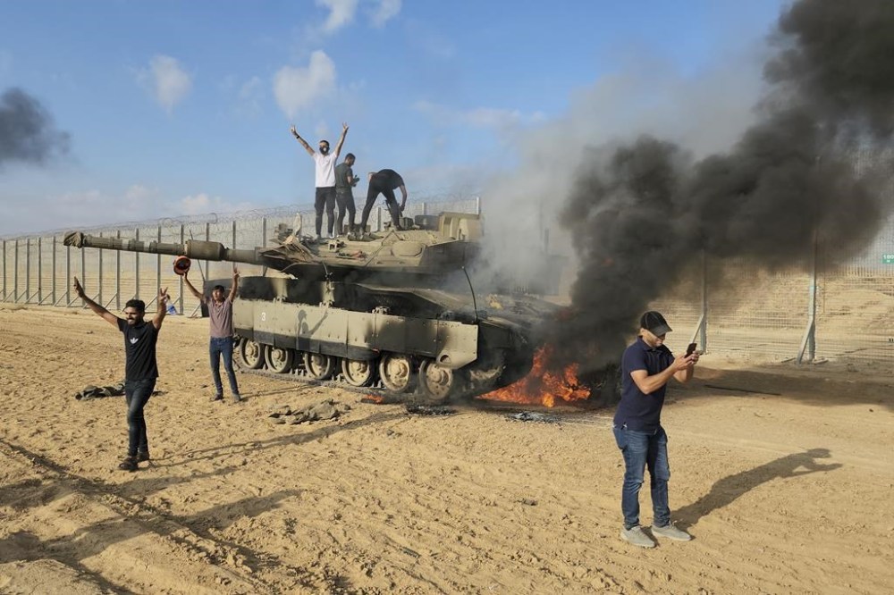 Palestinians celebrate by a destroyed Israeli tank at the Gaza Strip fence east of Khan Younis Saturday, Oct. 7, 2023. The militant Hamas rulers of the Gaza Strip carried out an unprecedented, multi-front attack on Israel at daybreak Saturday, firing thousands of rockets as dozens of Hamas fighters infiltrated the heavily fortified border in several locations by air, land, and sea and catching the country off-guard on a major holiday. (AP Photo/Hassan Eslaiah)