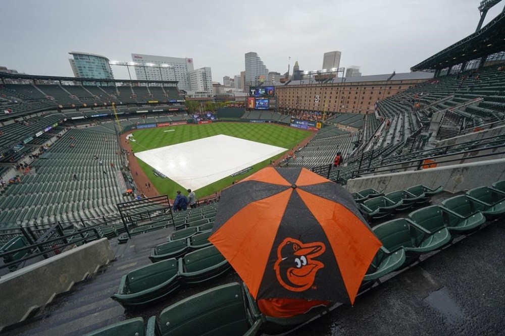 A fan sits in the stand with an umbrella as they wait for the start of Game 1 of an American League Division Series baseball game between the Baltimore Orioles and the Texas Rangers, Saturday, Oct. 7, 2023, in Baltimore, Md. (AP Photo/Julio Cortez)