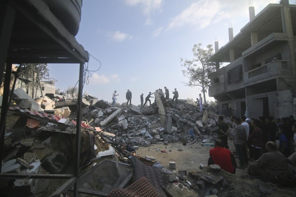 Palestinians stand by the building destroyed in an Israeli airstrike in Rafah, Gaza Strip, Saturday, Oct. 14, 2023. (AP Photo/Hatem Ali)