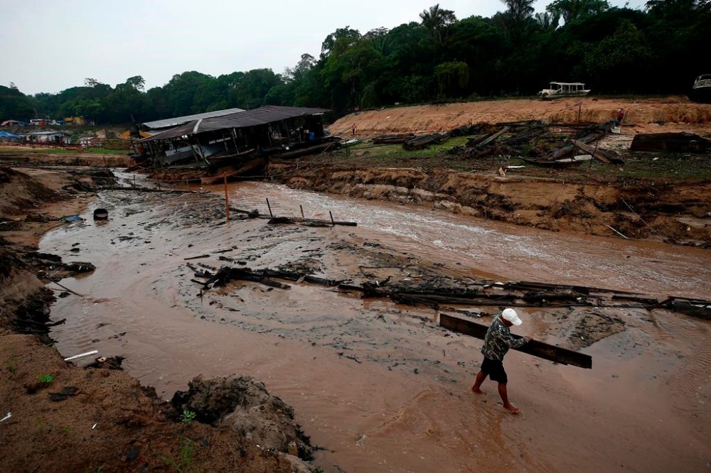 A resident carries wood to help dam up the Negro River river near his houseboat that is stuck in a dry area during a drought in Manaus, Amazonas state, Brazil, Monday, Oct. 16, 2023. The Amazon’s second largest tributary on Monday reached its lowest level since official measurements began near Manaus more than 120 years ago. (AP Photo/Edmar Barros)