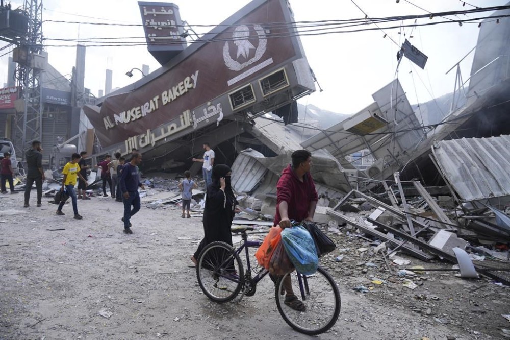 An Ontario man says his father, who's stuck in Gaza, is on the brink of starvation along with other relatives and is calling on the international community to push Israel to allow humanitarian aid into the enclave immediately. Palestinians walk by the destroyed building of Al Nuseirat Bakery in an Israeli airstrike Nusseirat refugee camp Gaza Strip, Wednesday, Oct. 18, 2023. THE CANADIAN PRESS/AP-Hatem Moussa