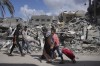 Palestinians walk next to the buildings destroyed in Israeli airstrikes in Bureij refugee camp, Gaza Strip, Wednesday, Oct. 18, 2023. (AP Photo/Hatem Moussa)