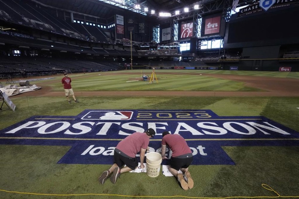 Members of the Chase Field grounds crew put the finishing touches on a MLB sign on the field Wednesday, Oct. 18, 2023, in Phoenix as the Arizona Diamondbacks and Philadelphia Phillies prepare to play Game 3 in the baseball NL Championship Series on Thursday. (AP Photo/Ross D. Franklin)