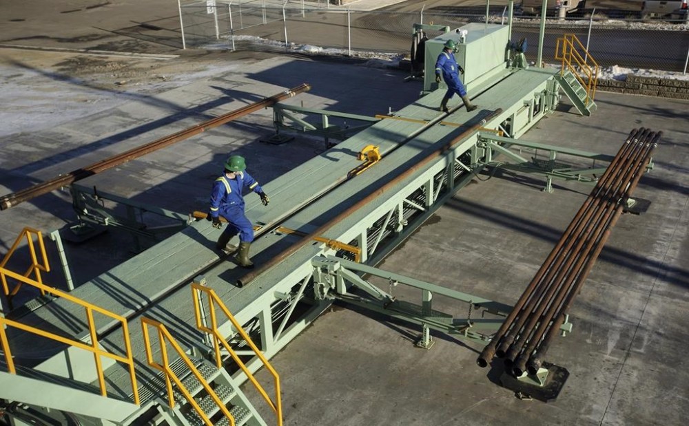 Trainees roll pipe off a catwalk during a training session to lay down drill pipe on a rig floor at Precision Drilling in Nisku, Alta., on Friday, January 20, 2016. THE CANADIAN PRESS/Jason Franson