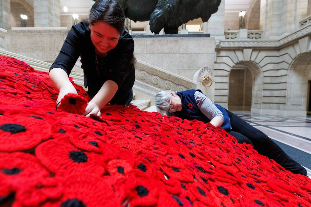 Poppy Blanket creator, Sheila Lee Restall (left) and Susan Wakeman (right), one of the volunteers that help maintain the Poppy Blanket, reattach handmade poppies to the blanket on the grand staircase. (Mike Deal / Winnipeg Free Press)