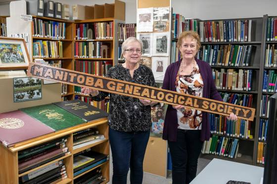 Gloria McNabb (left) and Daryl Dumanski are volunteers with the Manitoba Genealogical Society. The two are shown holding the society's wooden sign from its founding year in 1976. (Brook Jones / Winnipeg Free Press)