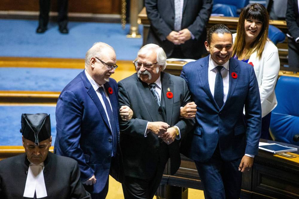 MIKAELA MACKENZIE / WINNIPEG FREE PRESS
Deputy Progressive Conservative leader Kelvin Goertzen (left) and Premier Wab Kinew drag new house Speaker Tom Lindsey to the chair, Thursday.