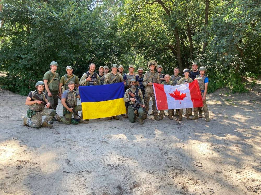 Supplied
Peter Derksen (centre) poses with Ukrainian and Canadian flags signed by soldiers from his brigade in summer 2023.