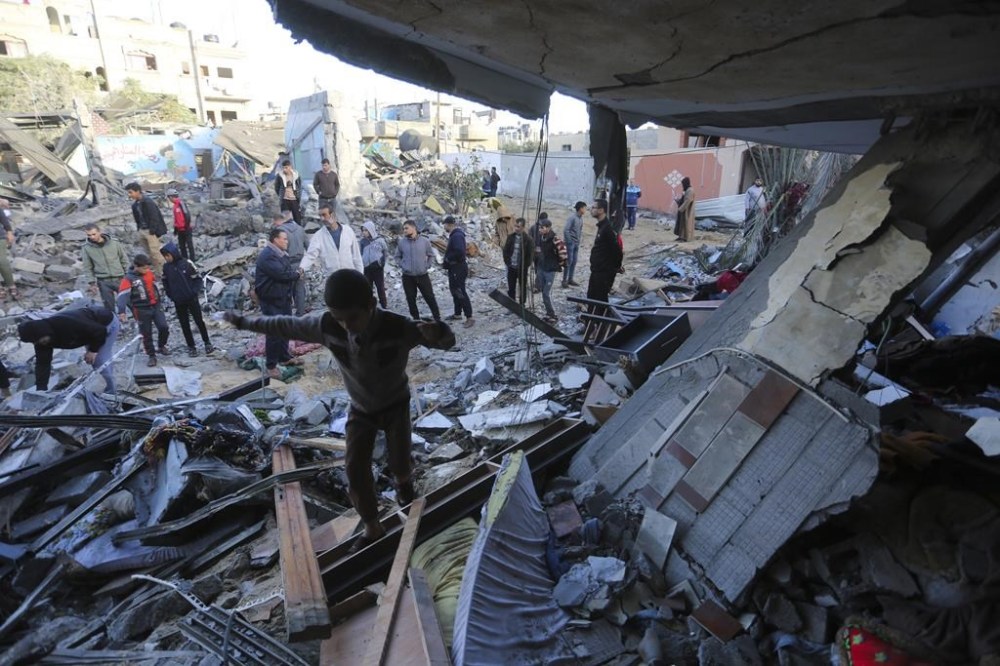 Palestinians stand by a building destroyed in Israeli bombardment overnight in Rafah, Gaza Strip, Friday, Nov. 24, 2023. (AP Photo/Hatem Ali)