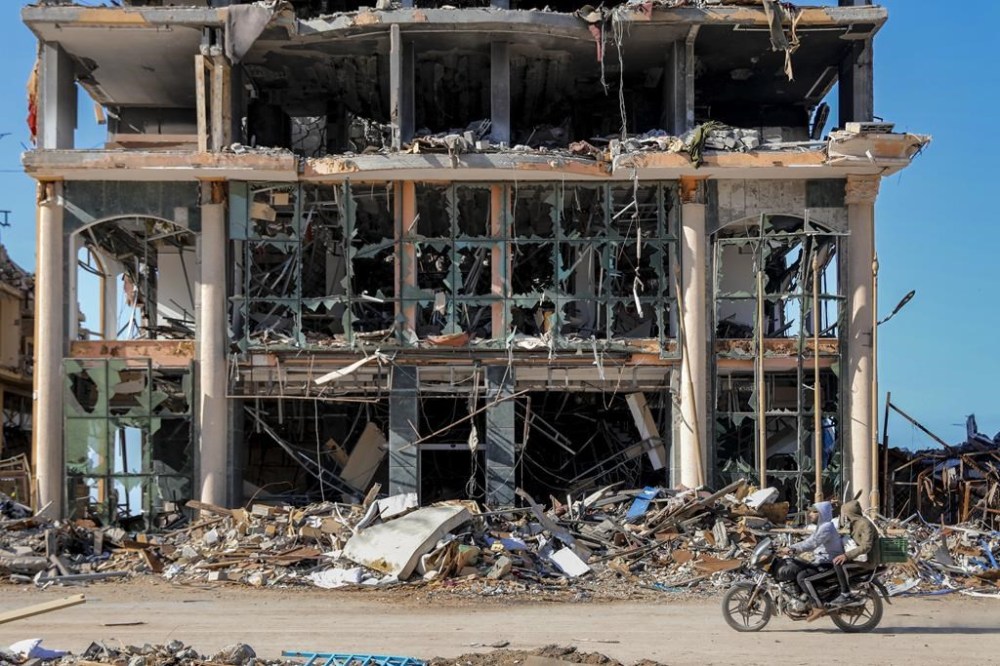 Palestinians ride a motorcycle by a destroyed building in Gaza City on Wednesday, Nov. 29, 2023, the sixth day of the temporary ceasefire between Hamas and Israel. International mediators on Wednesday worked to extend the truce in Gaza, encouraging Hamas militants to keep freeing hostages in exchange for the release of Palestinian prisoners and further relief from Israel's air and ground offensive.(AP Photo/Mohammed Hajjar)